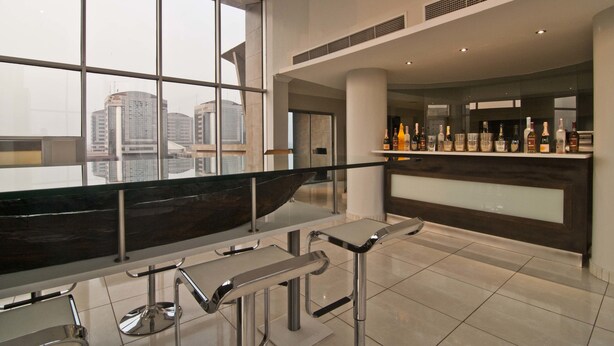 A modern bar area with a long counter, bar stools, and a view of the cityscape through large windows. - L'eola Suites (Abuja)