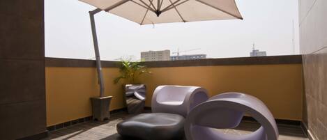 Terraza en la azotea con una sombrilla grande, asientos modernos y una planta en maceta.