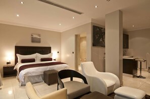 A modern hotel room with a large bed, a sitting area with chairs, a small table, and a bathroom with a sink and mirror. - L'eola Suites (Abuja)