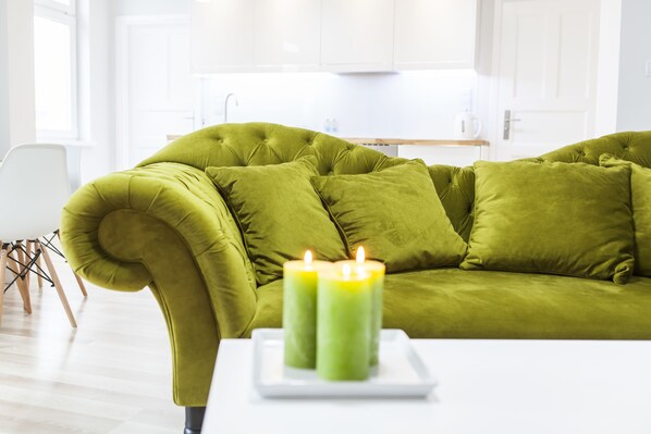 A green sofa with two lit candles on a white tray in a bright room with white cabinets and a wooden floor.