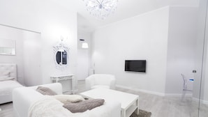 A modern, white-themed bedroom with a bed, two white sofas, a small table, a TV, and a chandelier. - Homewell Apartments Stara Piekarnia (Poznan)