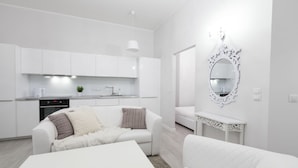A modern, white-themed living area with a sofa, a coffee table, and a dining table. A kitchen with white cabinets and a built-in oven is visible in the background. - Homewell Apartments Stara Piekarnia (Poznan)