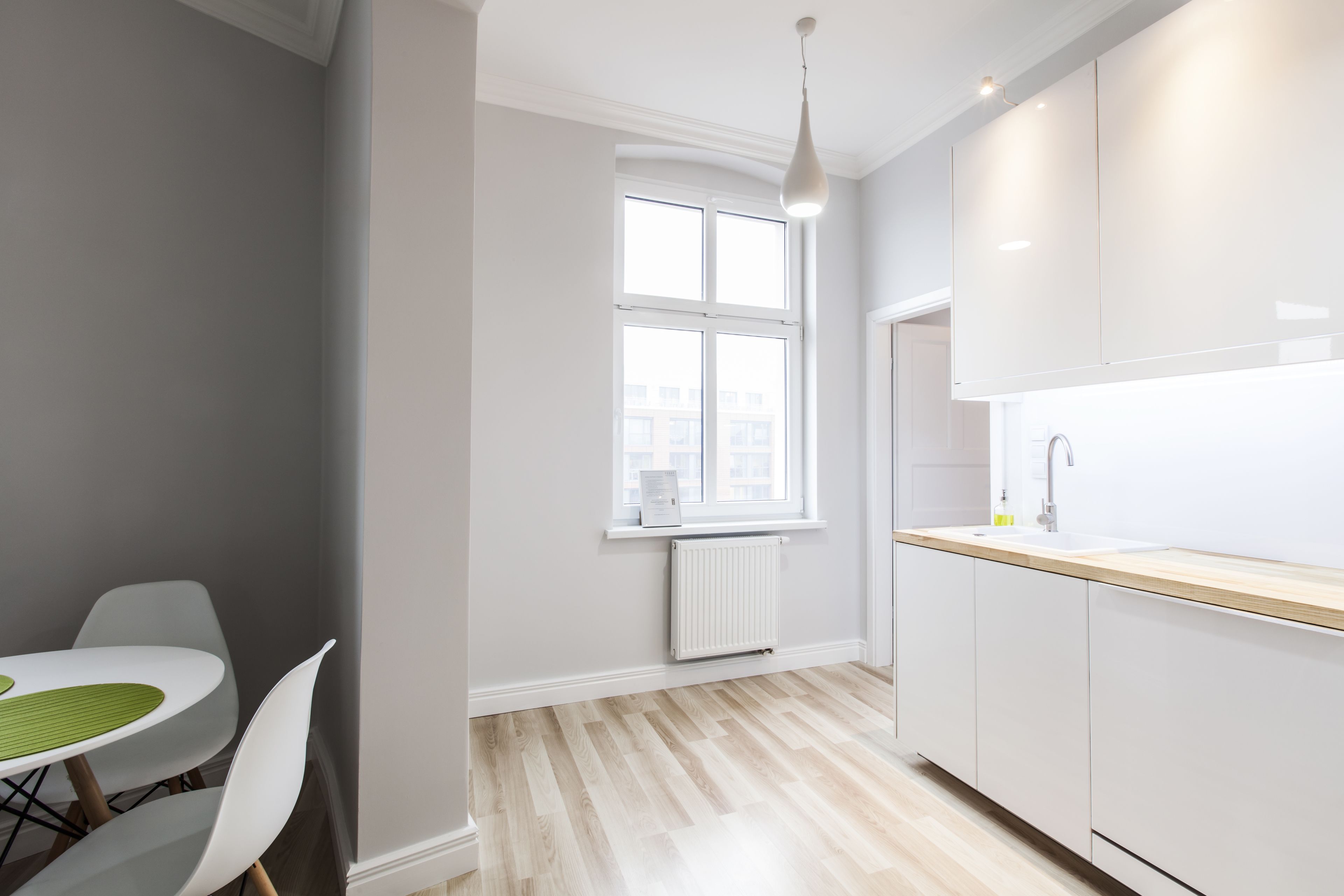 A modern kitchen with white cabinets, a wooden countertop, and a window with a view of buildings.