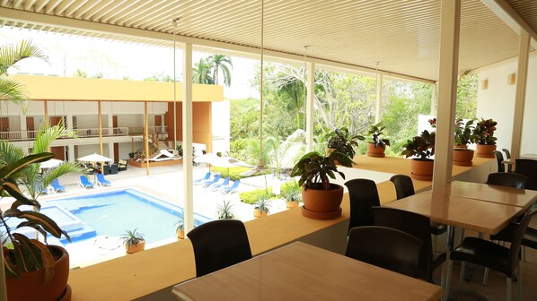 Un hotel con zona de piscina, mobiliario exterior y plantas en macetas.
