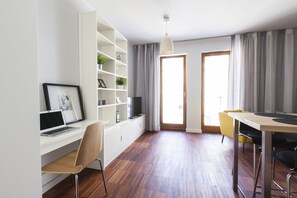A modern living space with a white desk, a laptop, a bookshelf, and a dining area with a table and chairs.