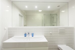 A modern bathroom with a large mirror, white tiles, a sink with two blue glasses, and a glass-enclosed shower.
