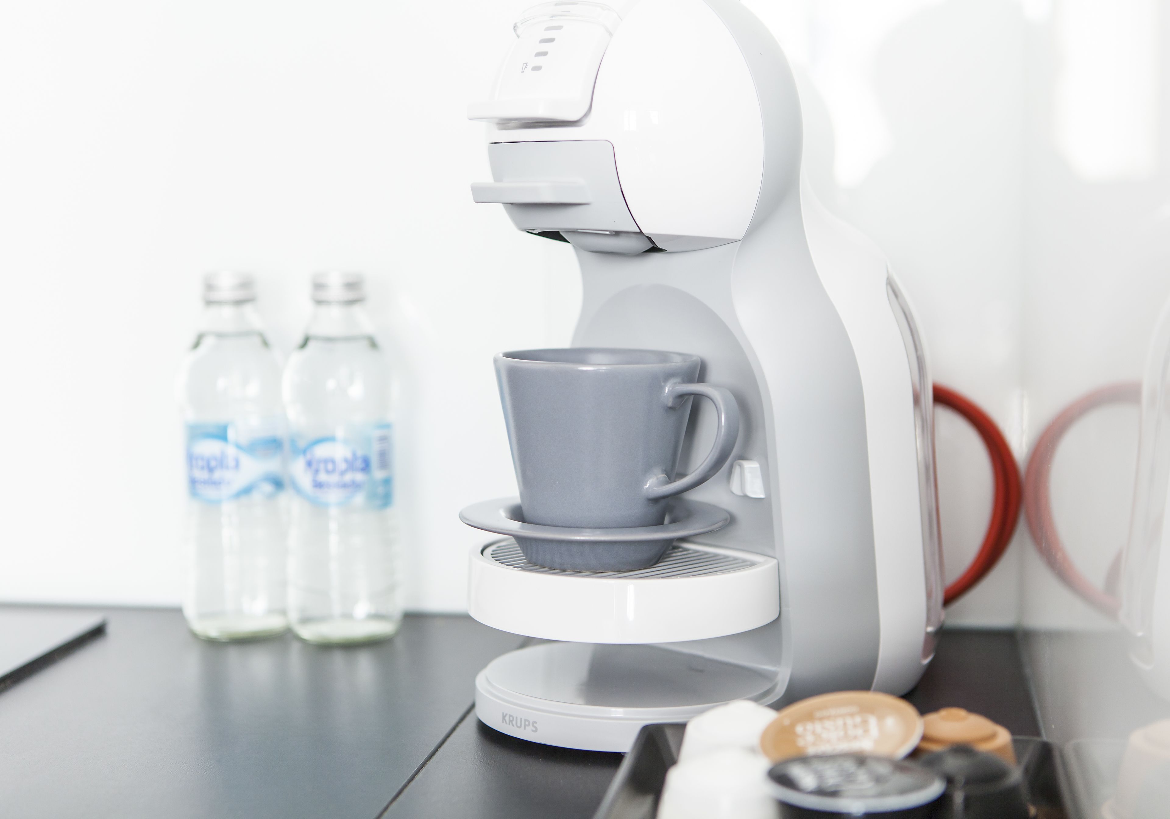 Une machine à café avec une tasse sur son socle, deux bouteilles d’eau et un plateau contenant une dosette de café et une cuillère.