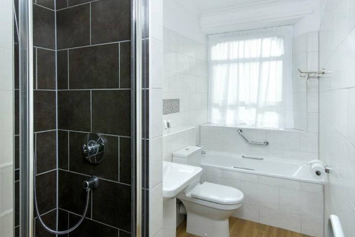 Un bany modern amb dutxa envidriada, un lavabo blanc, un vàter i una finestra amb cortines.