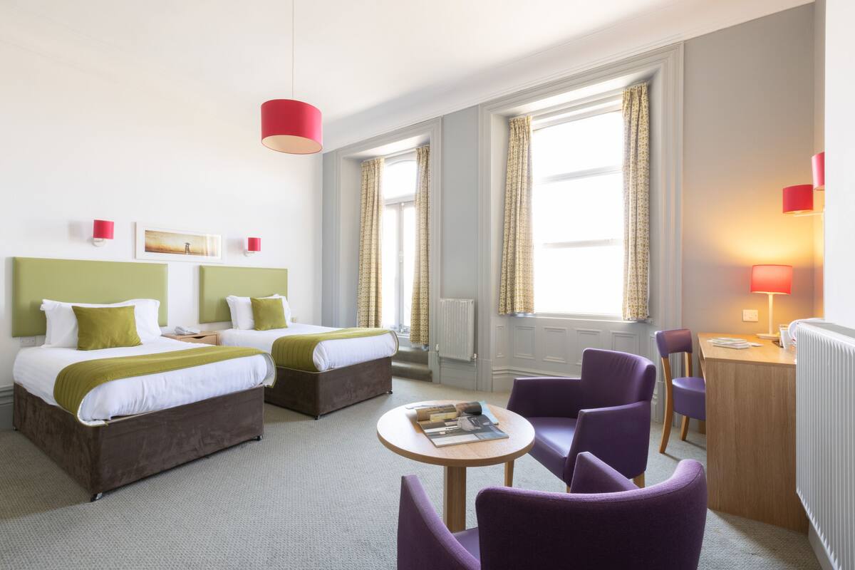 Habitació d'hotel amb dos llits, un escriptori, una cadira i una taula rodona.