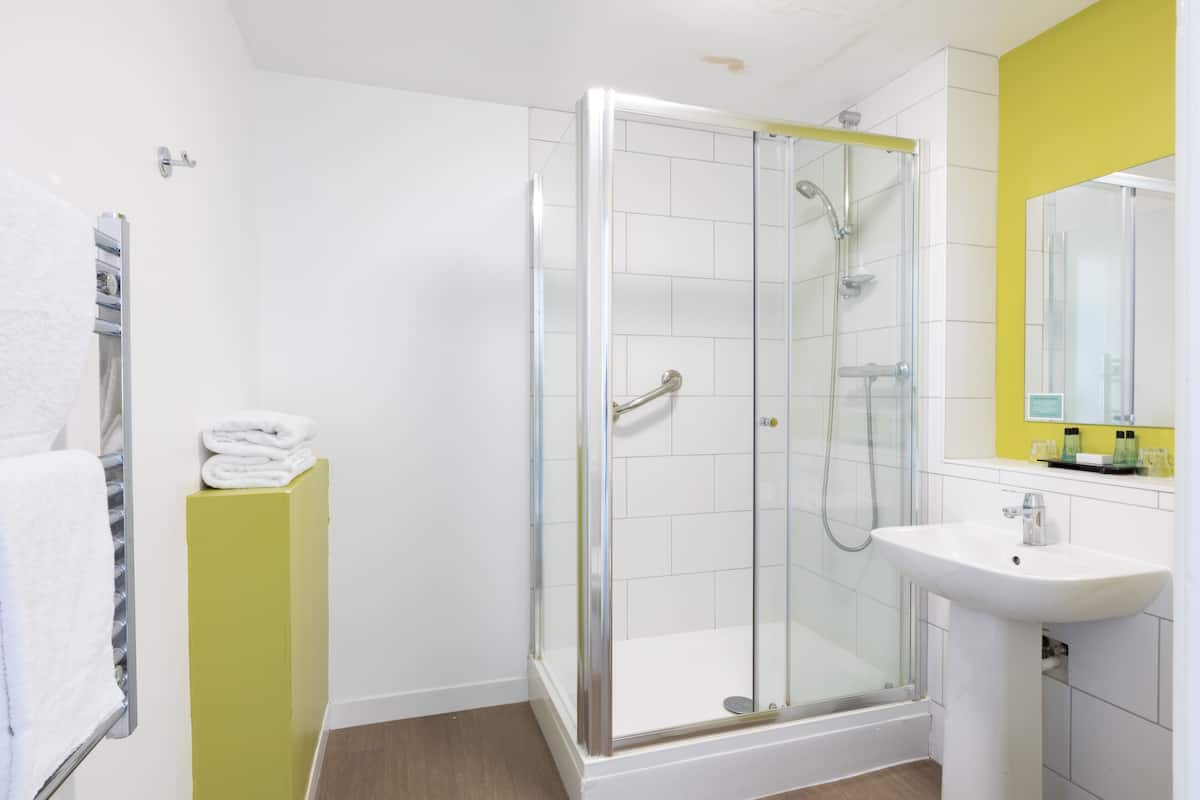 Un bany modern amb dutxa tancada amb vidre, un lavabo blanc i una paret d'accent groga.