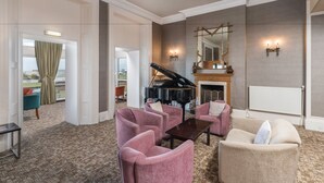 Un amplio salón con un piano de cola, asientos cómodos y una chimenea.