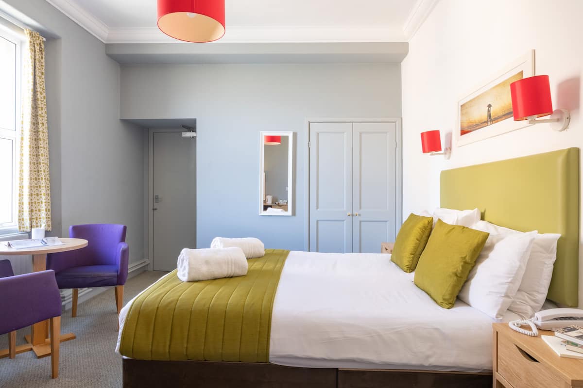 Habitació d'hotel amb un llit, una taula, una cadira i una finestra amb cortines.