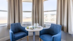 Una habitación con dos sillones azules, una mesa redonda pequeña y un ventanal con vista a un paisaje urbano.