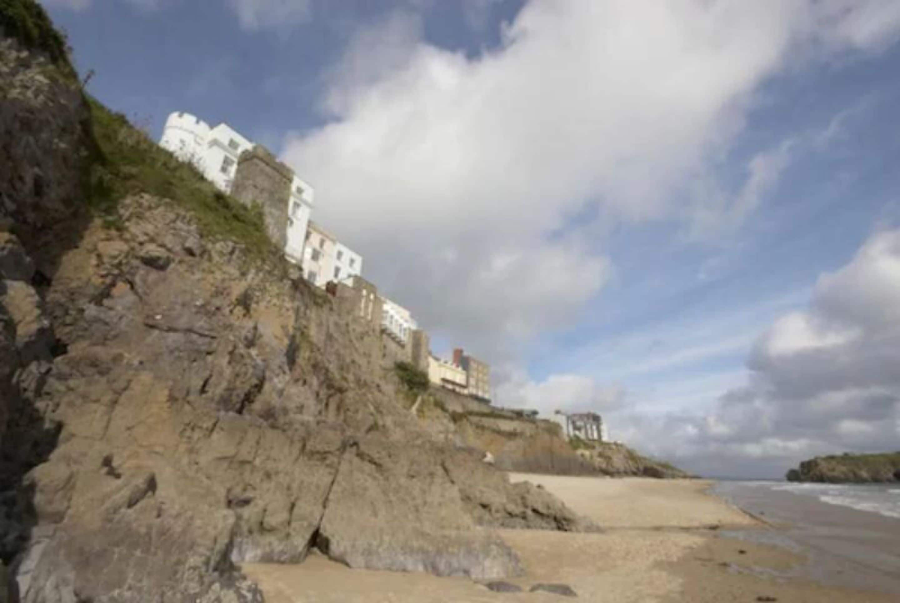 A coastal building with a rocky cliff, a sandy beach, and a view of the sea.