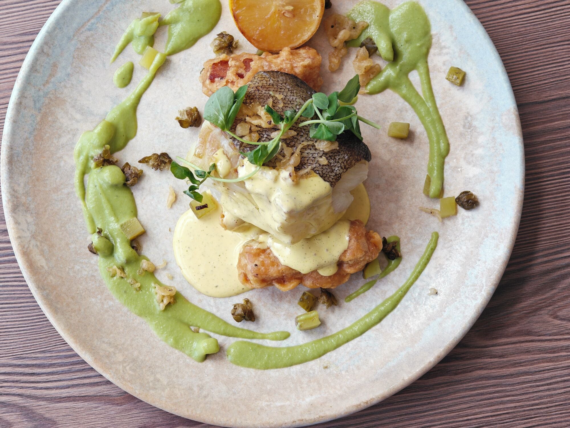 A plate with a fish dish, green sauce, and garnishes.