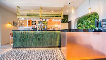 A reception area with a green-tiled counter, a patterned rug, and a green wall with plants.