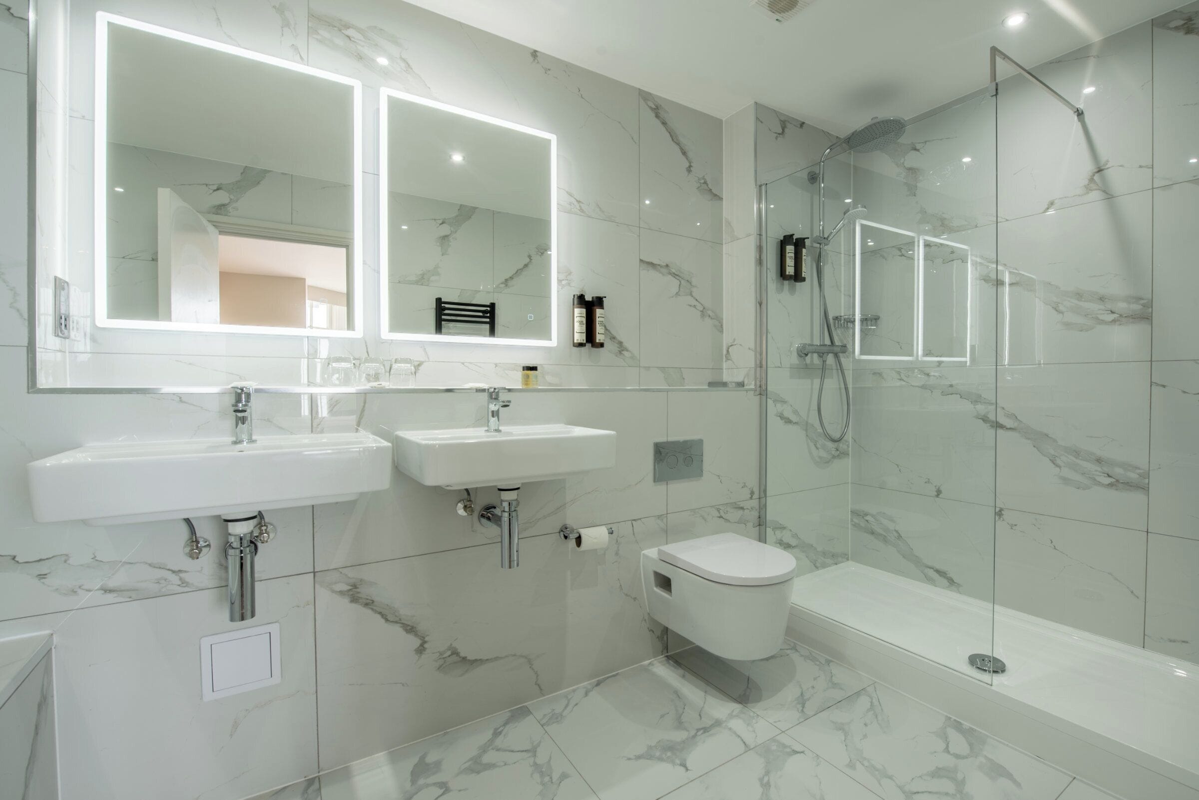 Une salle de bain moderne avec deux lavabos, des toilettes et une douche à parois de verre.