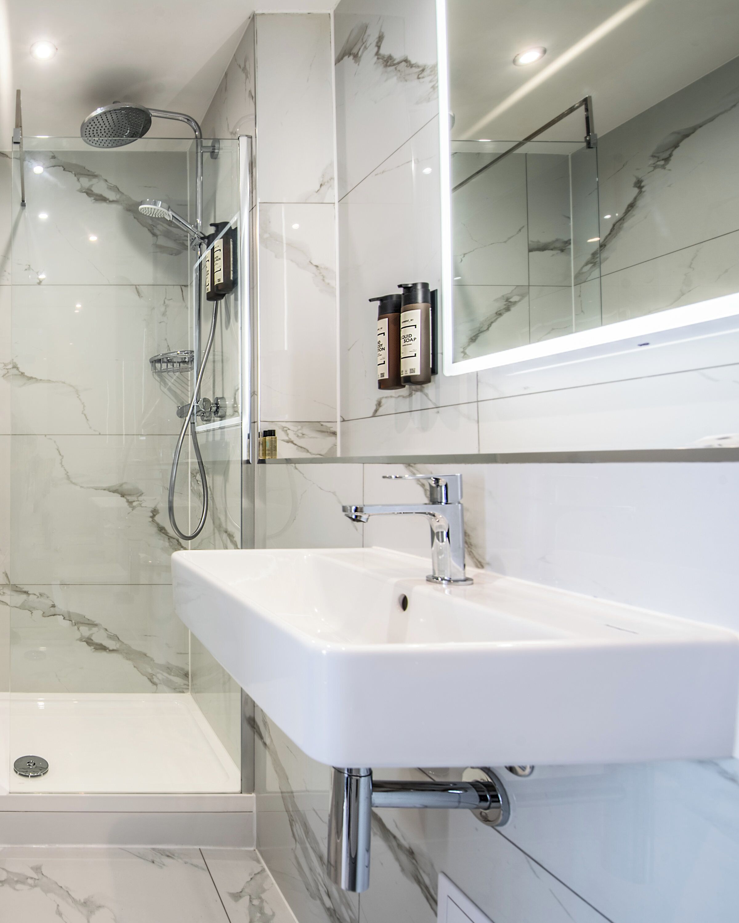 A modern bathroom with a glass-enclosed shower, a white sink, and marble tiles.