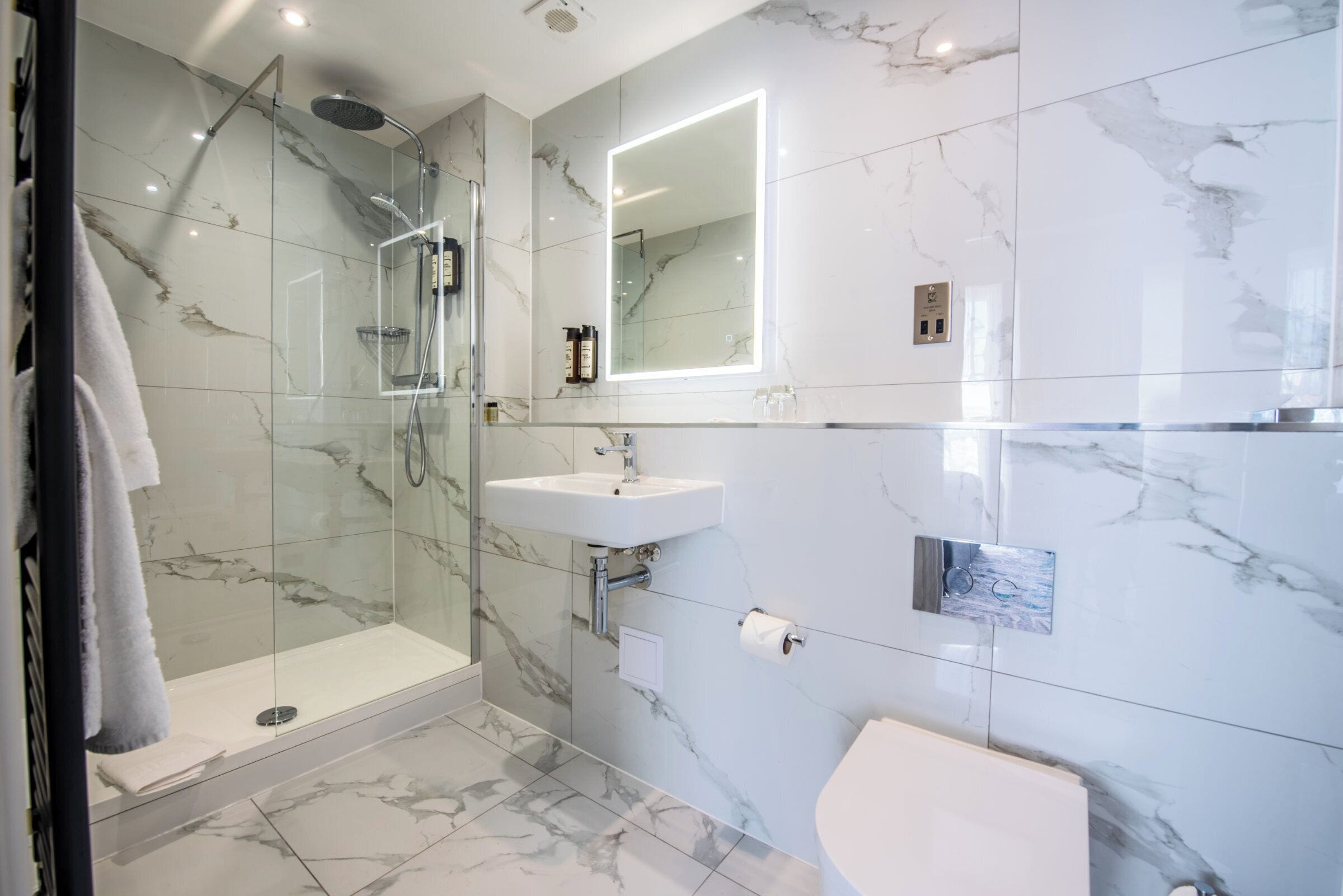 A modern bathroom with a glass-enclosed shower, a white sink, and a marble-tiled wall.
