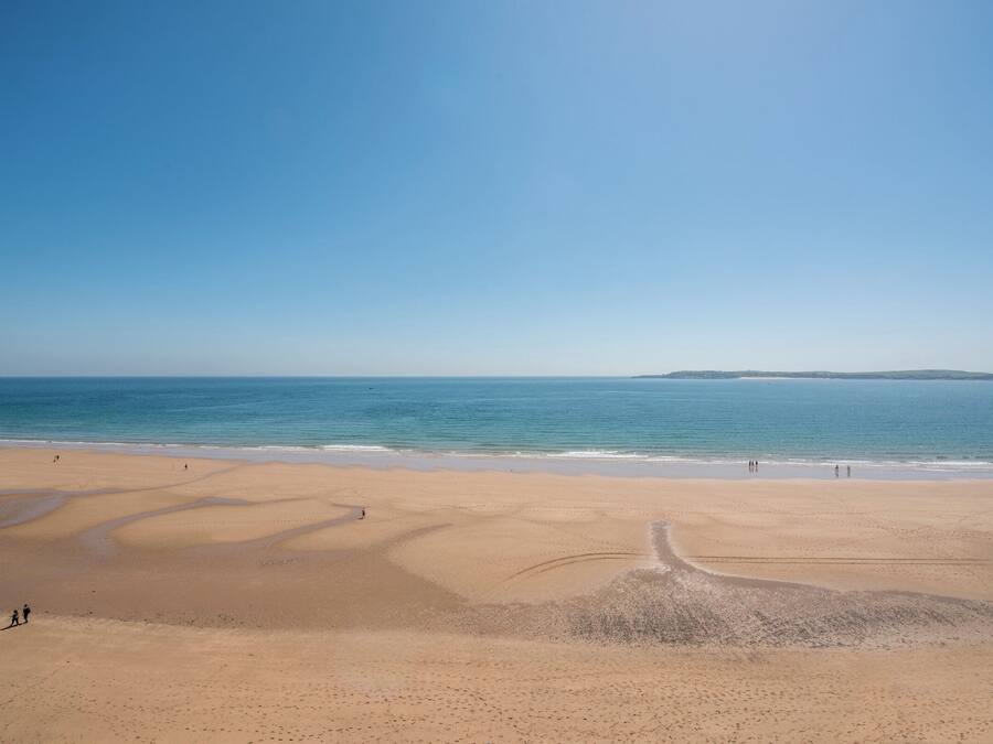 Une vaste plage de sable fin, avec des vagues douces, un ciel dégagé et des reliefs lointains.