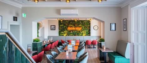 Ein modernes Restaurant mit einem langen Gemeinschaftstisch, roten und grünen Stühlen und einer grünen Wand mit dem Schriftzug 'Fresh from the Grill'.