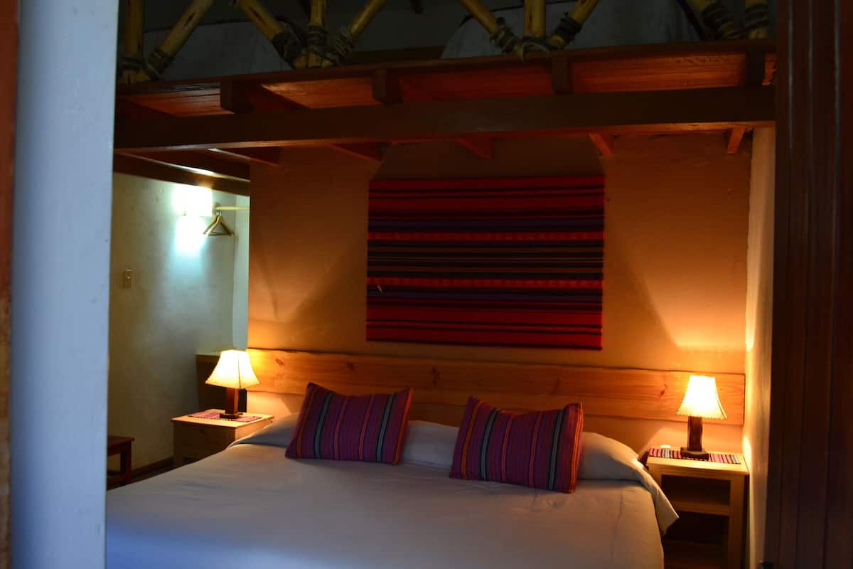 A hotel room with a large bed, two bedside lamps, and a wooden ceiling.