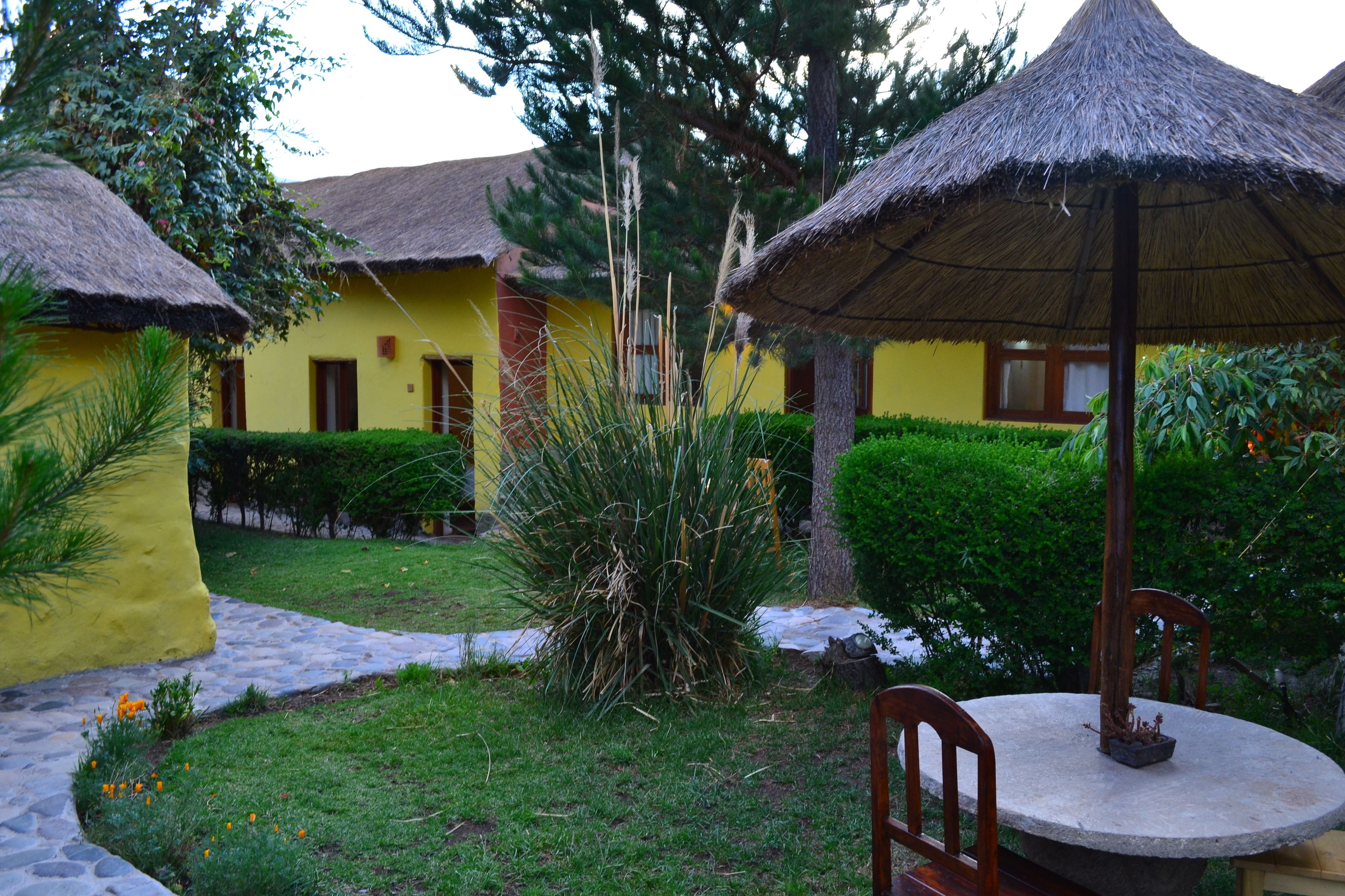 A courtyard with thatched-roof structures, a stone pathway, and a round table with chairs.