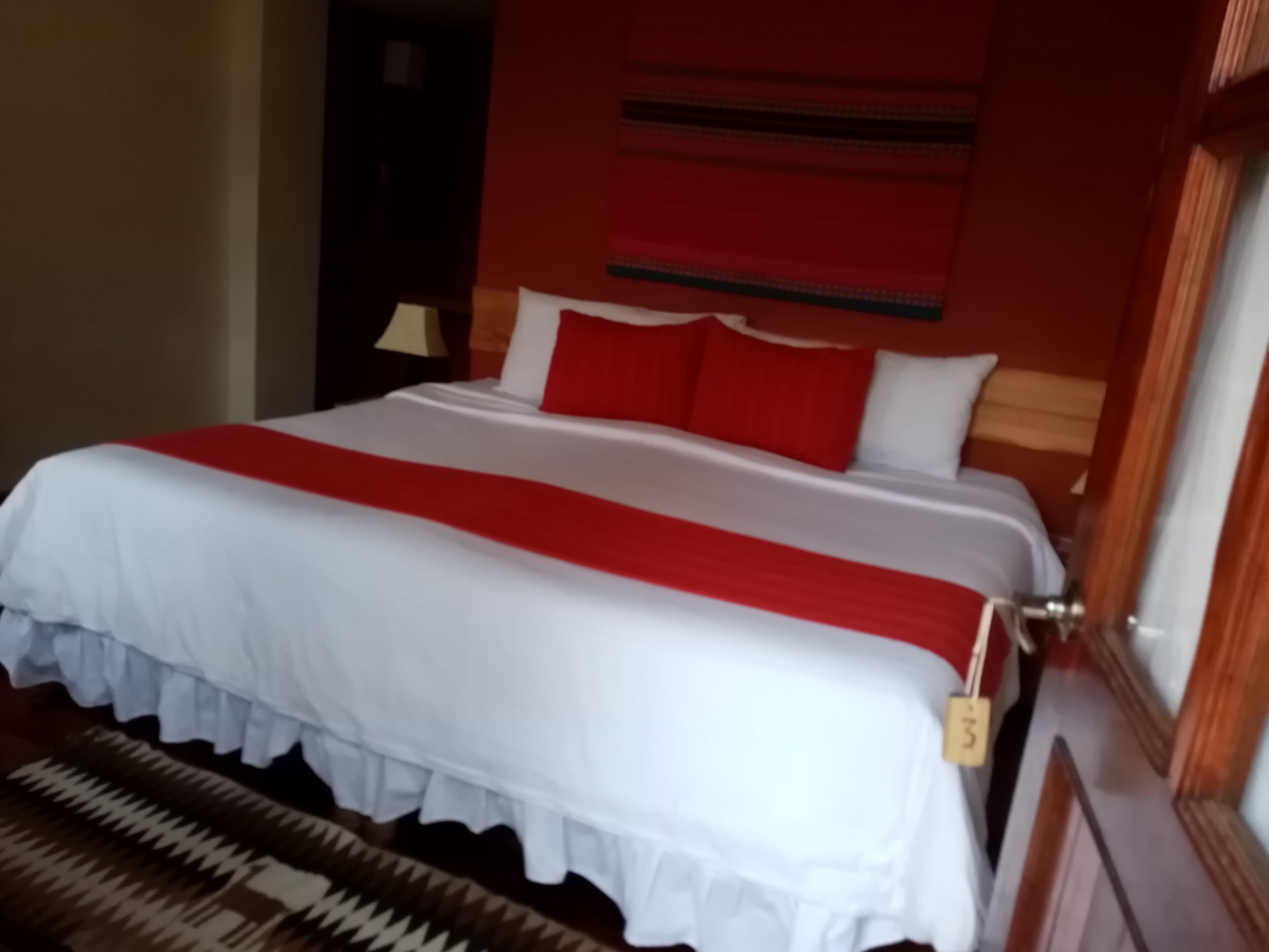 A bed with a white and red bedspread, a wooden headboard, and a red pillow.