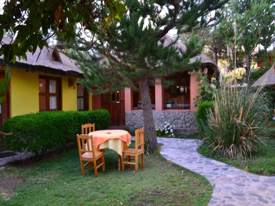 A courtyard with a table and chairs, a tree, and a building with a thatched roof.