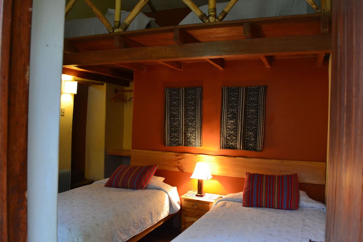 A room with two beds, wooden headboards, a nightstand with a lamp, and patterned wall decorations.