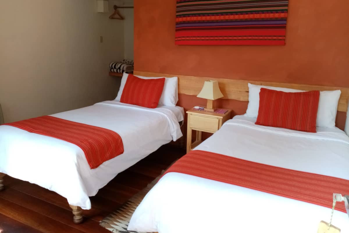 Two single beds with white and red bedding, wooden headboards, a nightstand with a lamp, and a striped wall hanging.