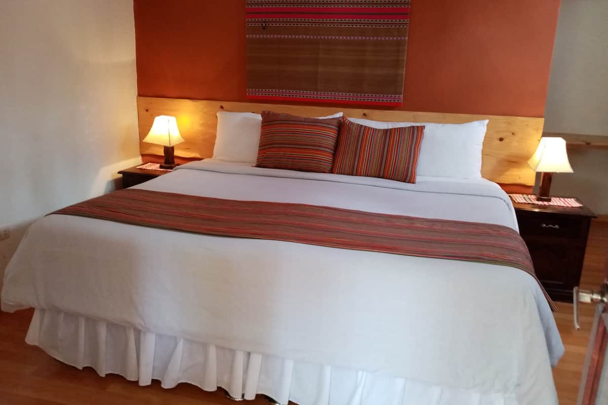 A neatly made bed with a white duvet and striped pillows, two bedside lamps, and a wooden headboard.