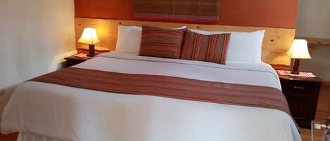 A neatly made bed with a white duvet and striped pillows, two bedside lamps, and a wooden headboard.