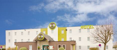 A B&B hotel with a flat facade, a green entrance, and a clear sky.