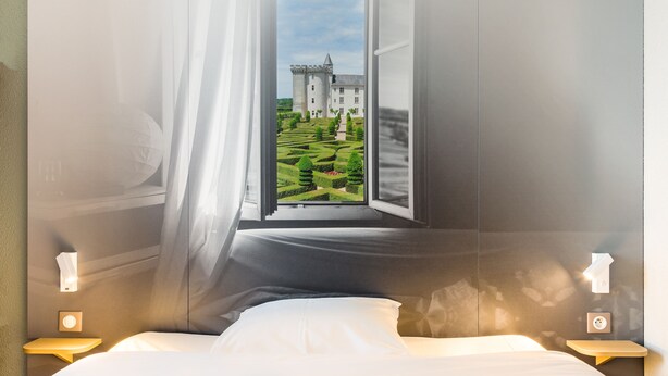 A bedroom with a large window offering a view of a castle and manicured garden. - B&B HOTEL Tours Nord 2 La petit Arche (Tours)
