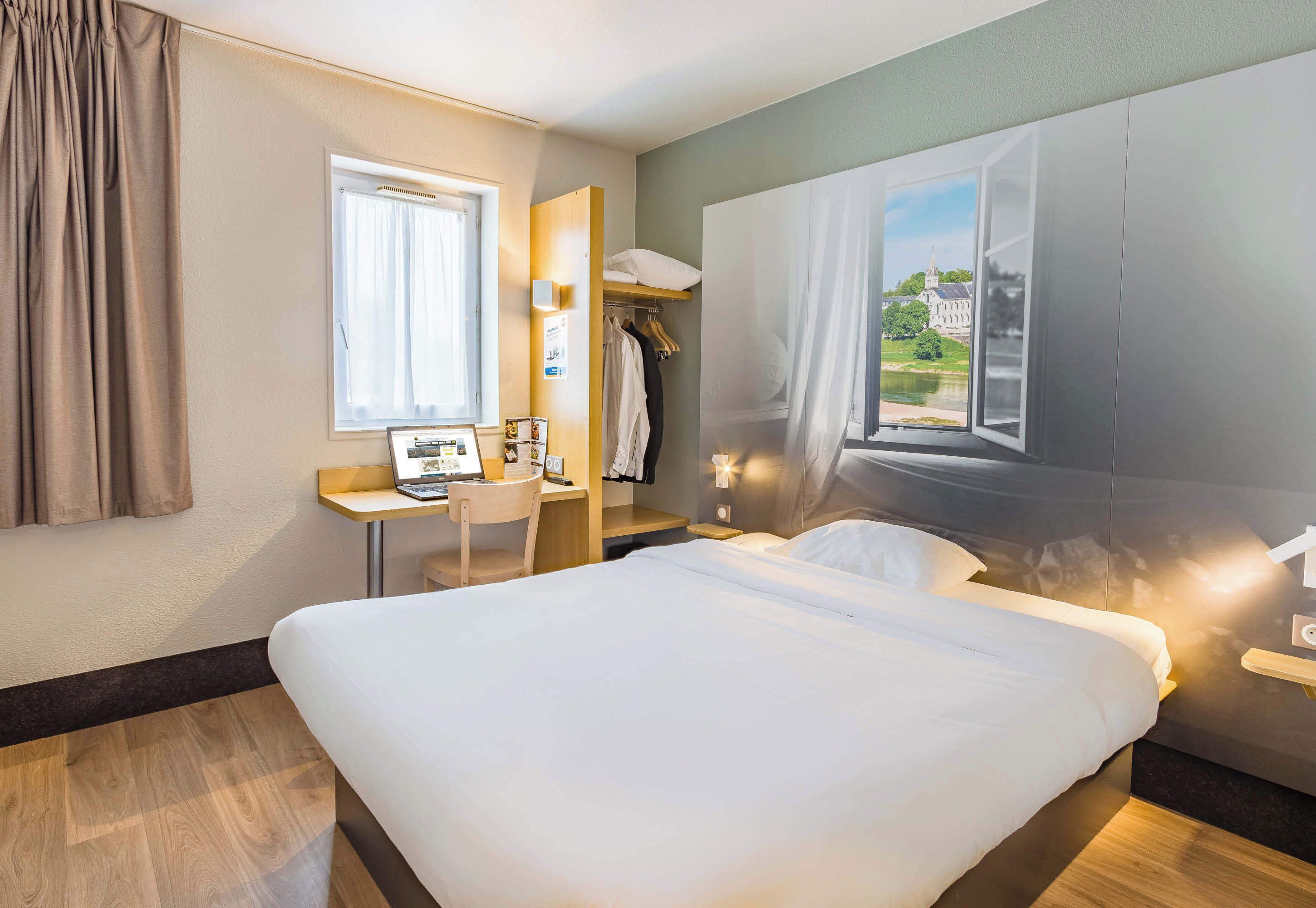 Quarto de hotel com cama, escrivaninha, cadeira, guarda-roupa e janela com vista.