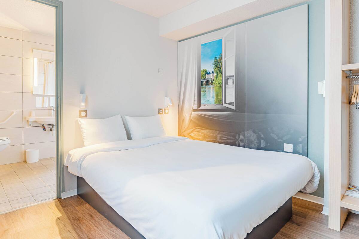 Una habitación de hotel moderna con una cama grande, un baño con ducha y vistas a un río a través de una ventana.