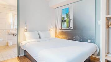 Una habitación de hotel moderna con una cama grande, un baño con ducha y vistas a un río a través de una ventana.