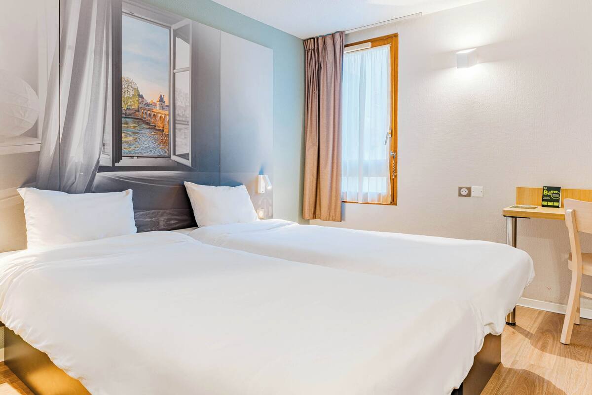 Habitación de hotel con dos camas, un escritorio y una ventana con vista a un puente.