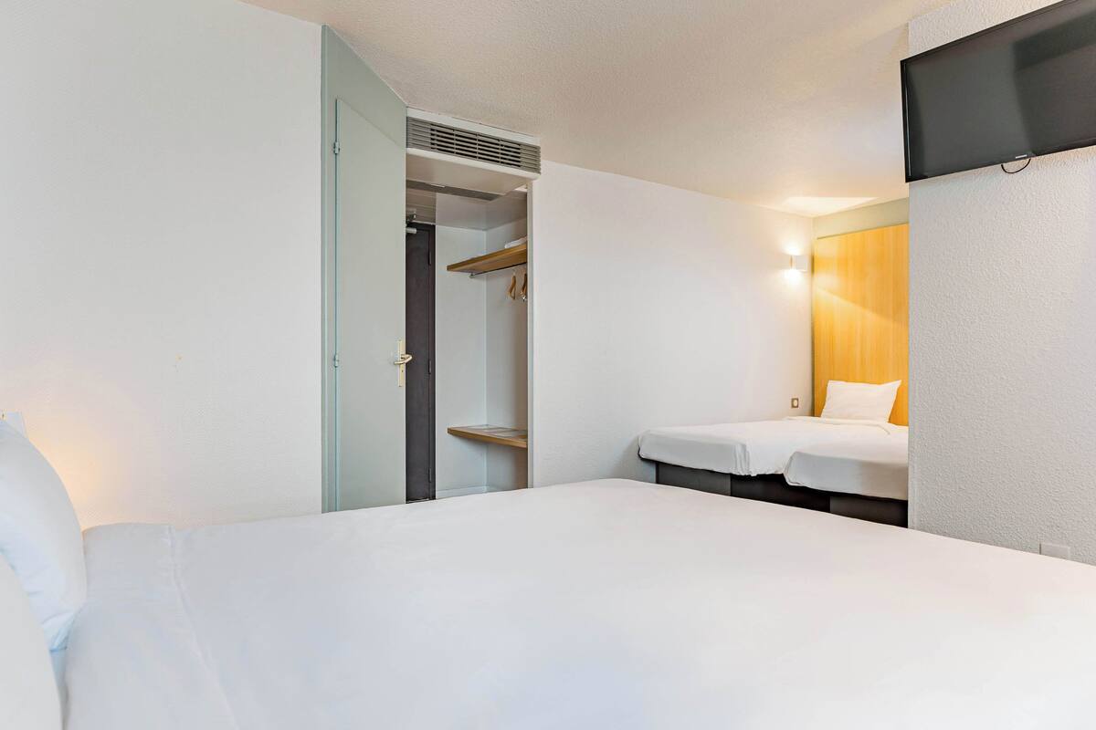 Una habitación de hotel con una cama, una mesita de noche, un armario y un televisor montado en la pared.