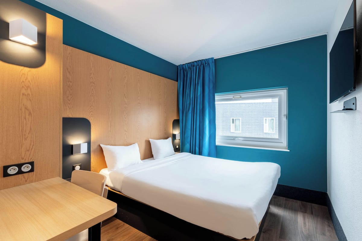 A hotel room with a bed, bedside table, and a window with curtains.