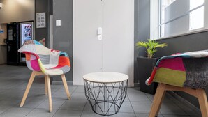 A room with a white door, a round table with a wireframe base, and two chairs with colorful upholstery. - B&B HOTEL Lille Roubaix Campus Gare (Roubaix)