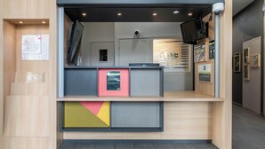 A reception area with a counter, a mounted TV, and framed informational posters. - B&B HOTEL Lille Roubaix Campus Gare (Roubaix)