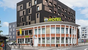 A modern hotel with a curved facade, multiple windows, and a prominent 'HOTEL' sign. - B&B HOTEL Lille Roubaix Campus Gare (Roubaix)