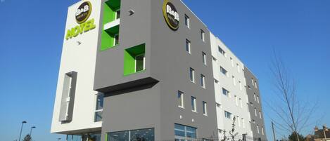 Un moderno edificio de hotel con fachada plana, grandes ventanales y un logotipo destacado en la parte lateral.