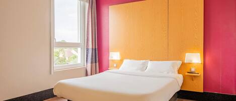Una habitación de hotel con una cama grande, dos lámparas de noche, una ventana con cortinas y un cabecero de madera.