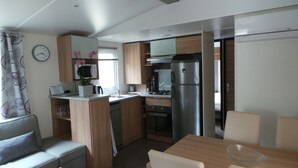 A compact kitchenette with a refrigerator, microwave, and stove. There is a dining area with a table and chairs. - Boost Locamobil 17 Bonne Anse Plage (Les Mathes)