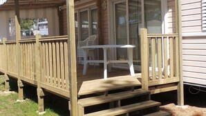 A wooden deck with a covered seating area, a table, and a bench. - Boost Locamobil 17 Bonne Anse Plage (Les Mathes)