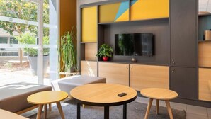 A modern office space with a large window, a flat-screen TV, and a seating area with round tables. - B&B HOTEL Lyon Caluire Cité Internationale (Caluire-et-Cuire)