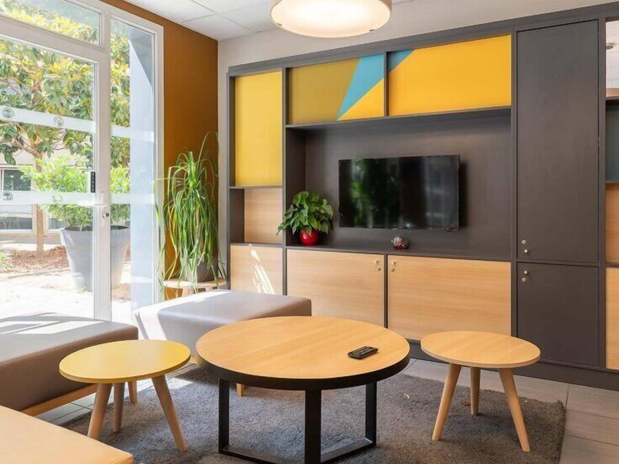 Een moderne kantoorruimte met een groot raam, een flatscreen televisie en een zithoek met ronde tafels.